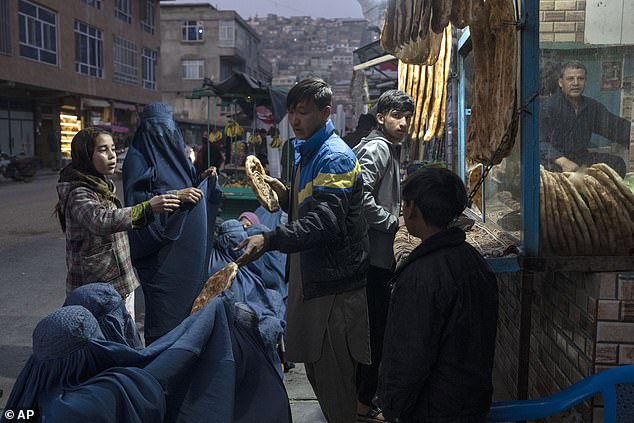 Một người đàn ông phát bánh mì cho phụ nữ Afghanistan bên ngoài một tiệm bánh ở thủ đô Kabul vào tháng 12, khi giá cả ở quốc gia này tăng cao kể từ khi Taliban nắm quyền kiểm soát. Ảnh: AP