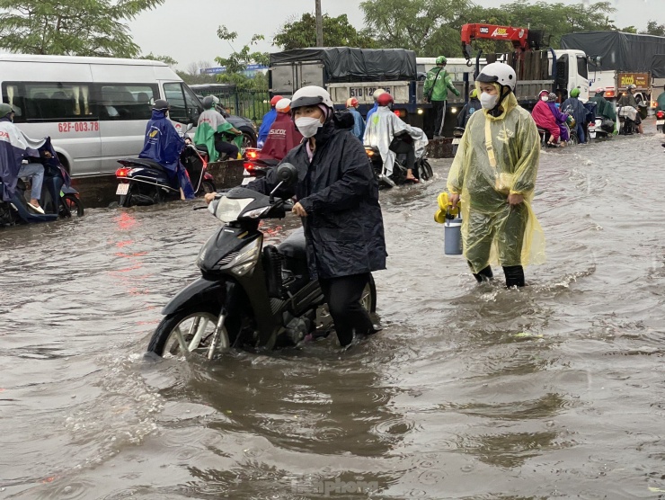 Người dân bì bõm dắt bộ phương tiện thoát khỏi điểm ngập trên quốc lộ 1 (quận Bình Tân).