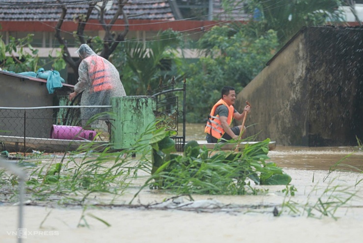 Một hộ dân tại huyện Lệ Thủy dùng thuyền chở đồ dùng sinh hoạt ra khỏi ngôi nhà nước ngập gần tới nóc.