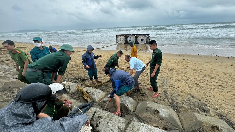 Lực lượng chức năng cùng người dân neo thùng kim loại vô chủ để đảm bảo an toàn, tránh tiếp tục trôi dạt. Ảnh: ĐC