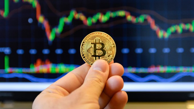 Nhà đầu tư đang cầm biểu trưng Bitcoin trước màn hình theo dõi thị giá. Ảnh: CNBC